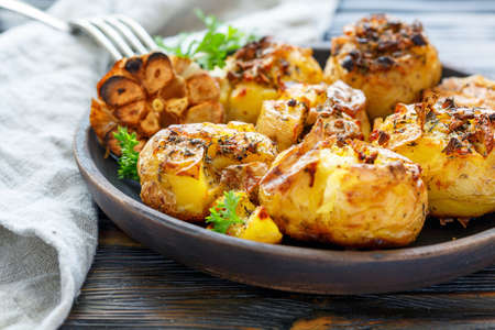 Baked potatoes in skin with spices, olive oil and garlic on a wooden dish, selective focus.の写真素材