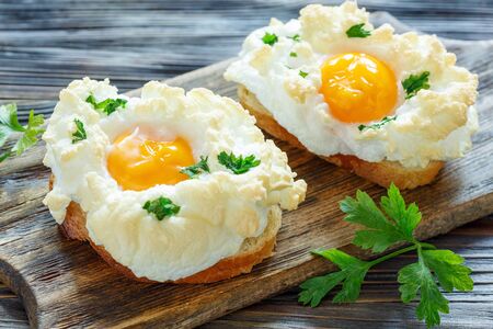Bread with baked eggs Orsini and parsley leaves on a wooden stand, selective focus.の写真素材