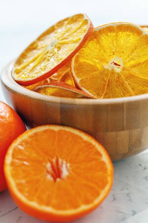 Dried slices of orange and lemon in wooden bowl on a white stone table, selective focus.の写真素材