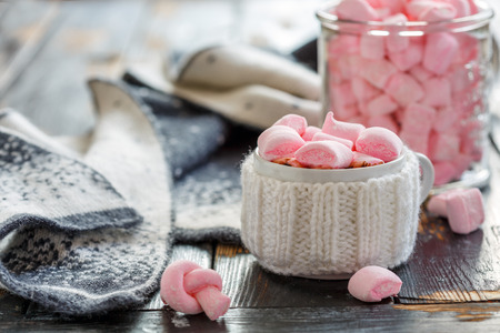Mug with hot chocolate and marshmallows on a wooden table with a warm scarf, selective focus.の写真素材