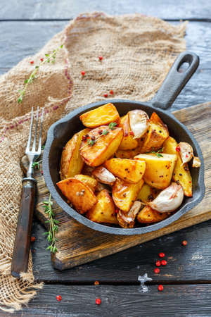 Cast iron skillet with baked potato slices, garlic, pepper and thyme on an old wooden table, selective focus.の写真素材