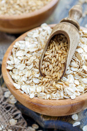 Bowl with oat flakes and wooden scoop on the old kitchen table, selective focus.