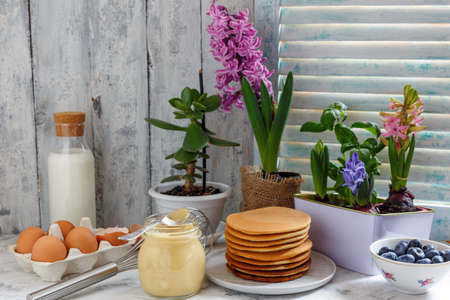 Pancakes on a plate, colorful hyacinths on a table in front of an old wooden window, selective focus.の写真素材