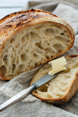 Cut loaf of french artisanal bread and a knife with butter on a linen cloth, selective focus.