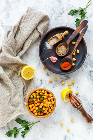 Appetizer of spicy chickpeas in a wooden bowl, cumin, chilli, garlic and lemon on a white concrete background.の写真素材