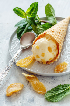 Waffle cone with artisanal ginger ice cream and a sprig of green mint on a white plate, selective focus.の写真素材