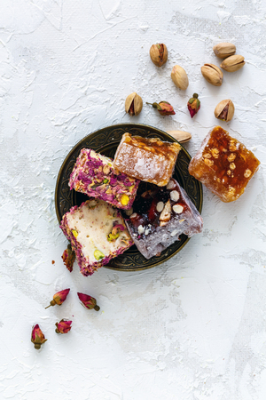 Plate with traditional oriental sweets rahat lukum, pistachios and dry roses on a white concrete background. View from the top.の写真素材