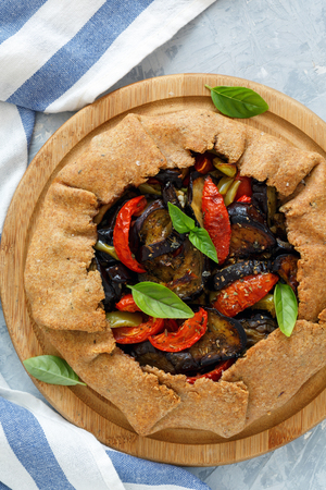 Homemade whole grain pie with eggplant, tomatoes and pepper on a wooden stand. View from the top.の写真素材