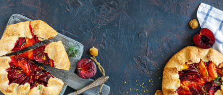 Homemade free-form pies (Galette) with yellow and red plums, rosemary, lemon zest on a dark textured background.の写真素材