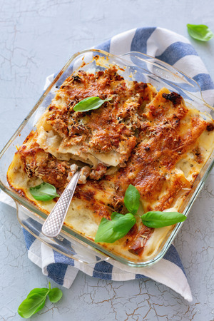 Cannelloni with minced meat and cream sauce in a glass pan on a linen cloth. Top view.の写真素材