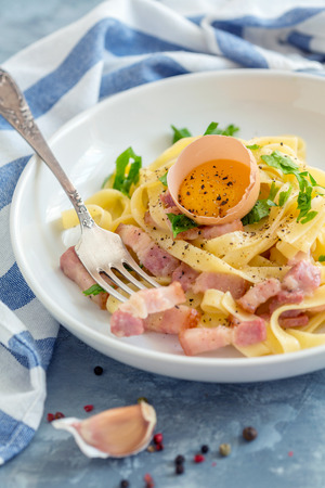 Plate of homemade pasta Carbonara and fork on a grey concrete background with a linen cloth, selective focus.の写真素材