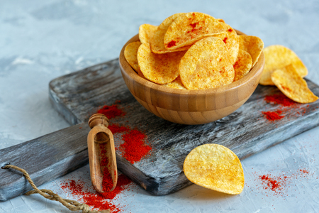 Bowl of paprika potato chips and a wooden scoop of ground paprika on an old serving board, selective focus.の写真素材