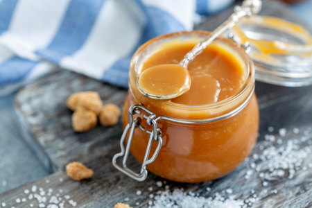 Small jar with homemade caramel sauce on a wooden serving board, selective focus.の写真素材