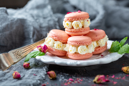 Plate of macarons with white cream roses, green mint and pink buds on a dark background, selective focus.の写真素材