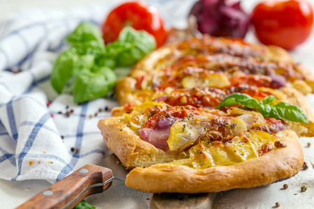 Sliced homemade pie with potatoes, onions, tomatoes and herbs on a textured white table, selective focus.の写真素材
