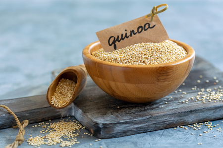 Bowl with white quinoa on an old wooden serving board, selective focus.の写真素材