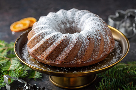 Homemade gingerbread cake sprinkled with powdered sugar on a dark background with fir branches and cookie cutters, selective focus.の写真素材