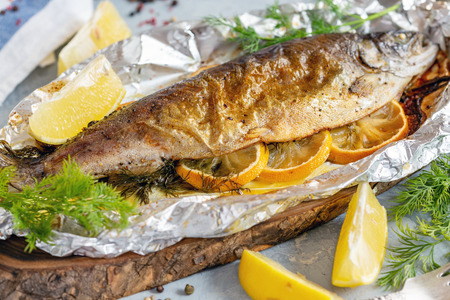 Trout with lemon slices and fresh dill baked in foil on a wooden serving board, selective focus.の写真素材