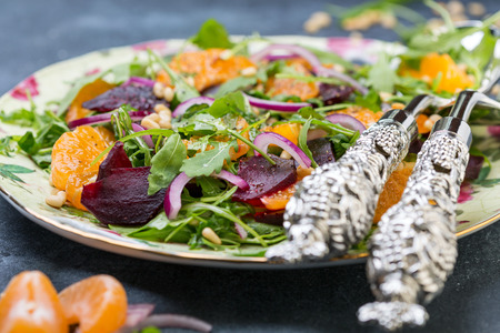 Salad of baked beetroot, arugula, red onion, tangerines and pine nuts on a platter with cutlery for salad close-up, selective focus.の写真素材
