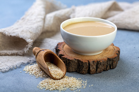 Ceramic bowl with tahini and white sesame seeds on textured gray background, selective focus.の写真素材