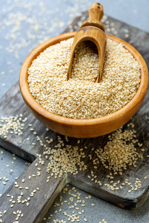 White sesame seeds and scoop in a wooden bowl on an old serving board, selective focus.の写真素材