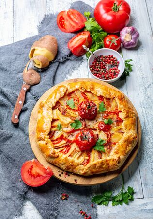 Delicious open pie (Galette) with potatoes, bacon, onions and tomatoes on a wooden serving board. Top view.の写真素材