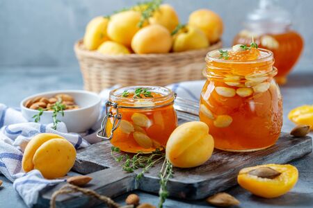 Homemade apricot jam with almonds and thyme in small glass jars on a wooden serving board, selective focus.の写真素材