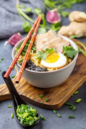 Ramen noodles with meat, egg, nori and green onions in a bowl on a textured gray background, selective focus.の写真素材