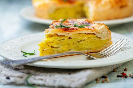 Plate with a piece of French puff pastry with potatoes on a white wooden table close-up, selective focus.の写真素材