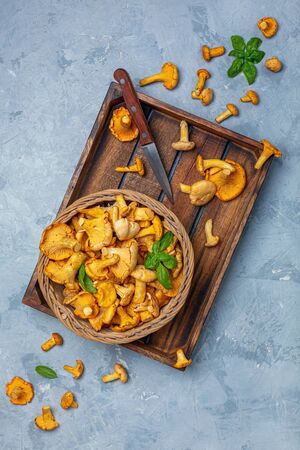Wicker basket with forest chanterelles and a knife in a wooden box on a gray textured background. Top view.の写真素材