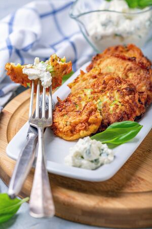 Zucchini pancakes with cottage cheese sauce and green basil on a plate, selective focus.の写真素材