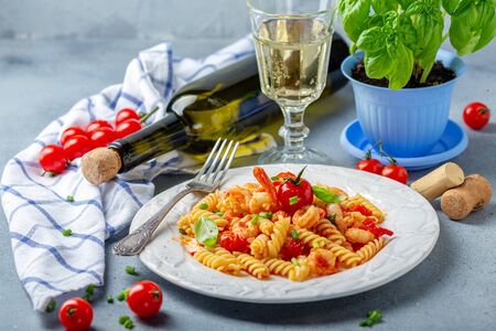 Fusilli pasta with shrimp in tomato sauce and a glass of white homemade wine on a textured gray table, selective focus.の写真素材