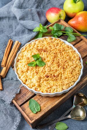 Apple crumble with cinnamon in white ceramic shape on wooden box with homespun linen fabric on dark textured background.Top view.の写真素材