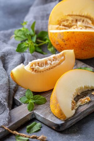 Ripe melon fruit cut into pieces on a wooden cutting board with homespun linen cloth on a dark textured background, selective focus.の写真素材