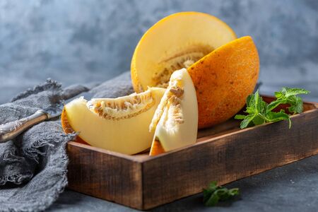 Fresh melon fruit cut into pieces in a wooden box with homespun linen cloth on a dark textured background.の写真素材