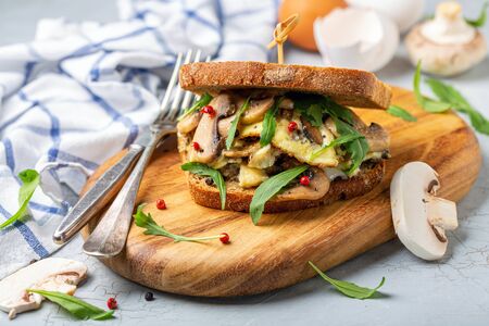 Breakfast sandwich with mushrooms, scrambled eggs and green arugula on a wooden serving board, selective focus.の写真素材