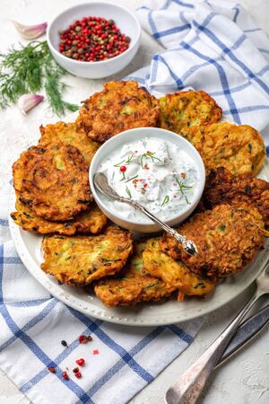 Zucchini fritters with spicy yogurt sauce are served on a ceramic dish on a homespun linen cloth.の写真素材
