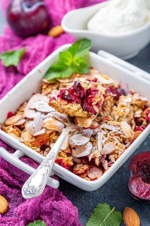 Plum crumble with oatmeal, almond flakes in a bowl close up on a dark textured background, selective focus.の写真素材