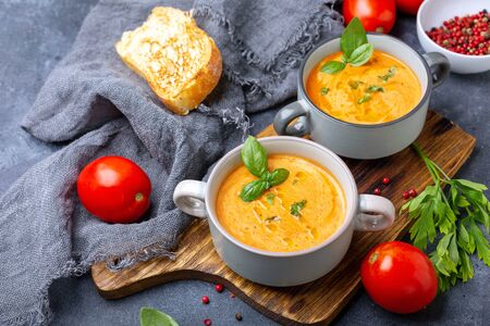 Homemade soup of fresh tomatoes, onions, garlic and herbs served with green basil in ceramic pots on a wooden serving board, selective focus.の写真素材