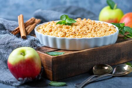 Apple crumbles in white ceramic shape on wooden box with homespun linen fabric on dark textured background, selective focus.の写真素材