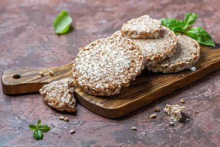 Puffed whole grain crispbreads and a sprig of green basil on a wooden serving board, selective...