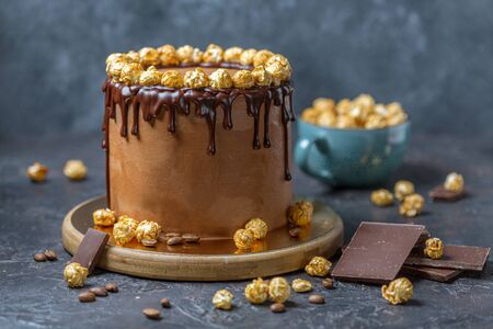 Chocolate and coffee cake with melting chocolate ganache and caramel popcorn decor on wooden stand on dark textured background, selective focus.の写真素材