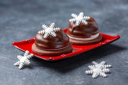 Marshmallow mini cakes in chocolate icing with Christmas decor on a red plate, selective focus.の写真素材