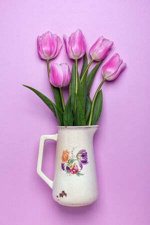 Spring tulips in a vintage jug on a pink background. Card for Valentine's day, birthday, mother's day, women's day. Top view, flat lay.の写真素材