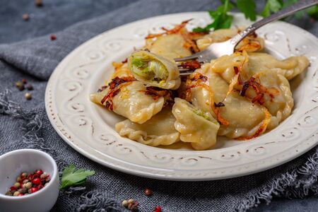 Homemade dumplings with cabbage filling are served with caramelized onions in a plate on a dark textured background, selective focus.の写真素材