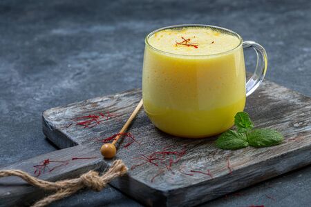 Trendy healthy food drink latte with saffron and almond milk in a glass cup served on a wooden serving board, selective focus.の写真素材