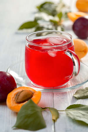 Sweet compote of plums and apricots is served in a glass cup with ice cubes, selective focus.