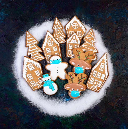 Funny ginger cookies in protective masks among gingerbread houses and fir trees. Concept of winter...