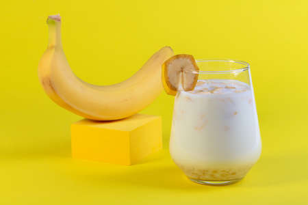 Traditional banana milk in a glass and ripe banana on yellow podium. Concept of a vegan alternative to traditional milk.の写真素材