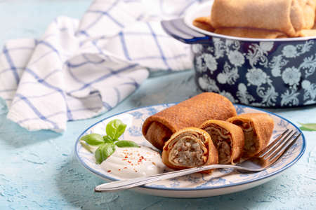 Homemade pancakes with minced meat are served with sour cream sauce. Concept of traditional home...